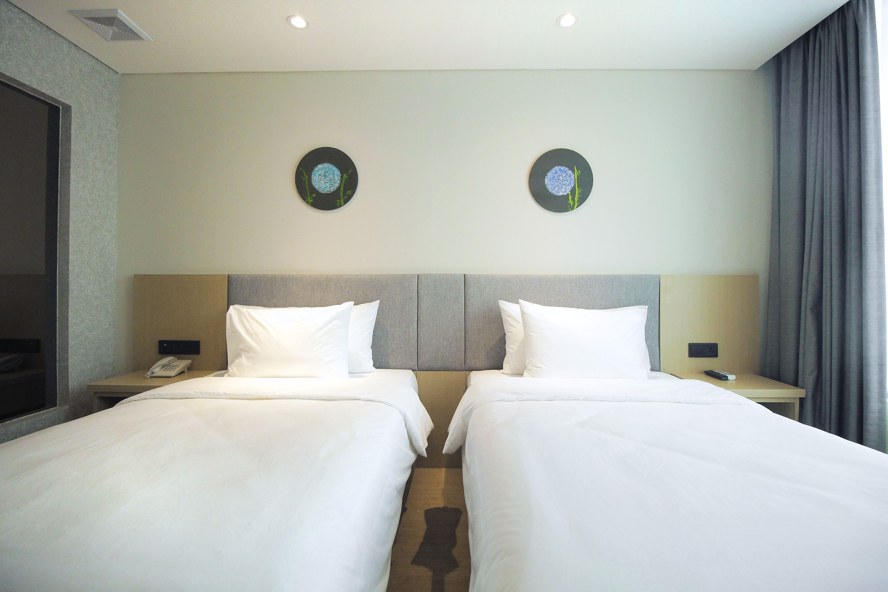 A hotel room with two beds, a headboard, bedside tables with lamps, a phone, and a window with curtains.