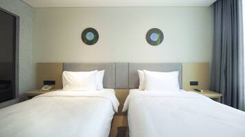 A hotel room with two beds, a headboard, bedside tables with lamps, a phone, and a window with curtains.