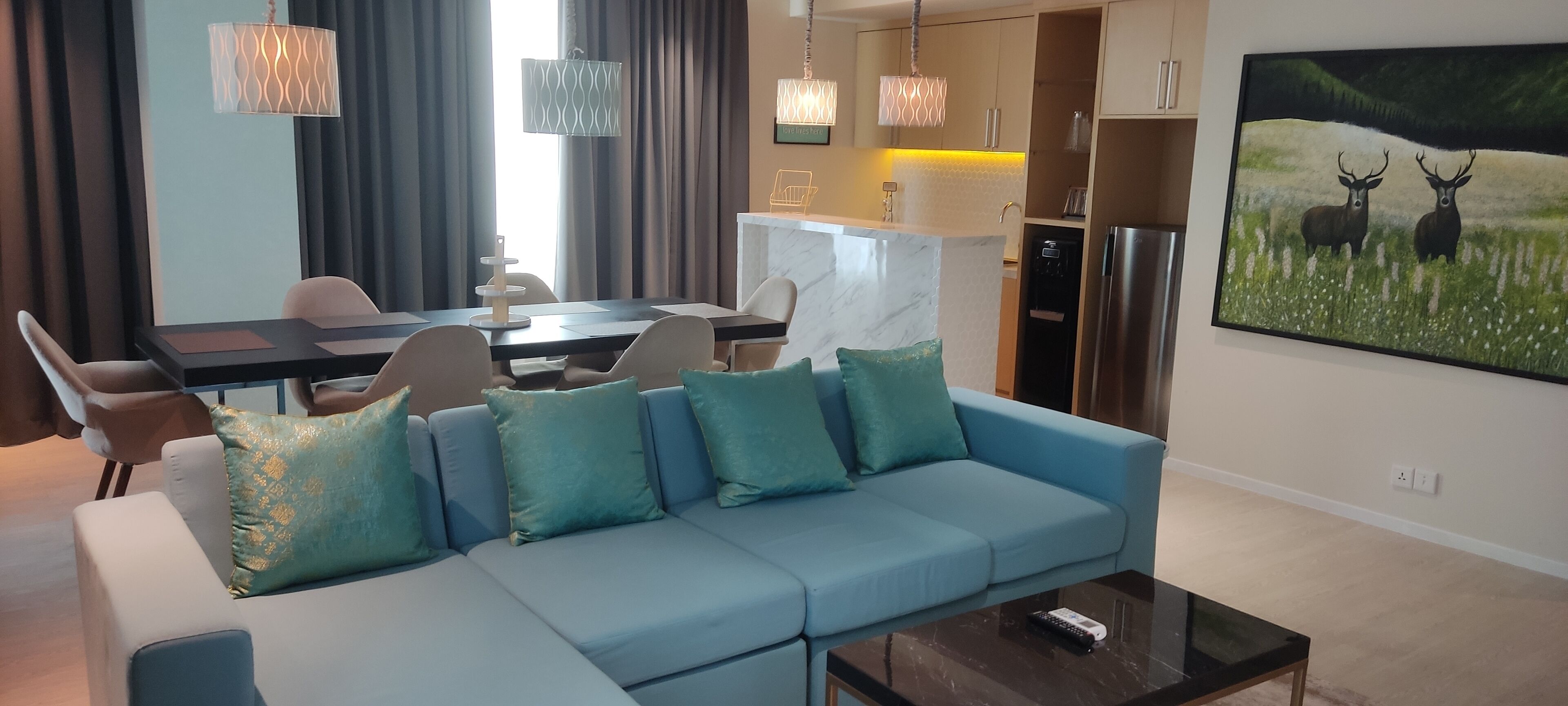 Un soggiorno moderno con un divano blu, una zona pranzo con tavolo e sedie, e una cucina con un piano di lavoro in marmo.
