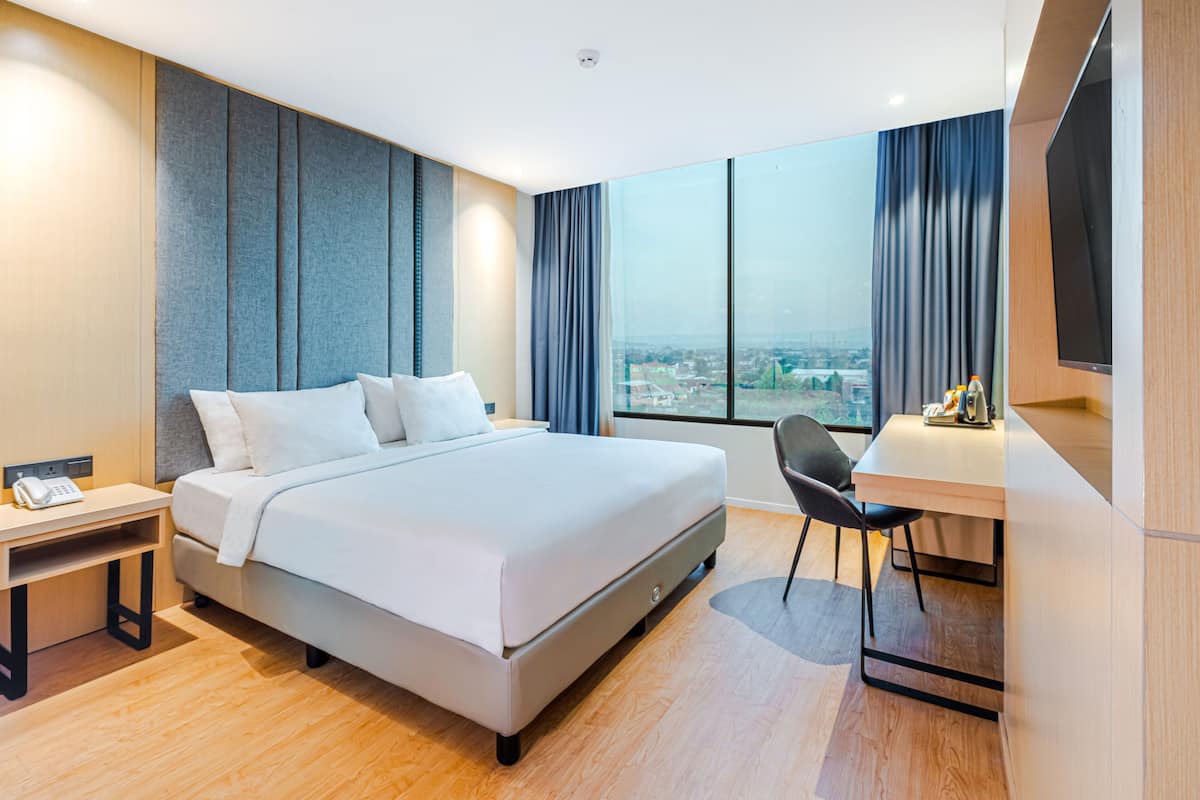 A modern hotel room with a large bed, a desk, and a view of the city.