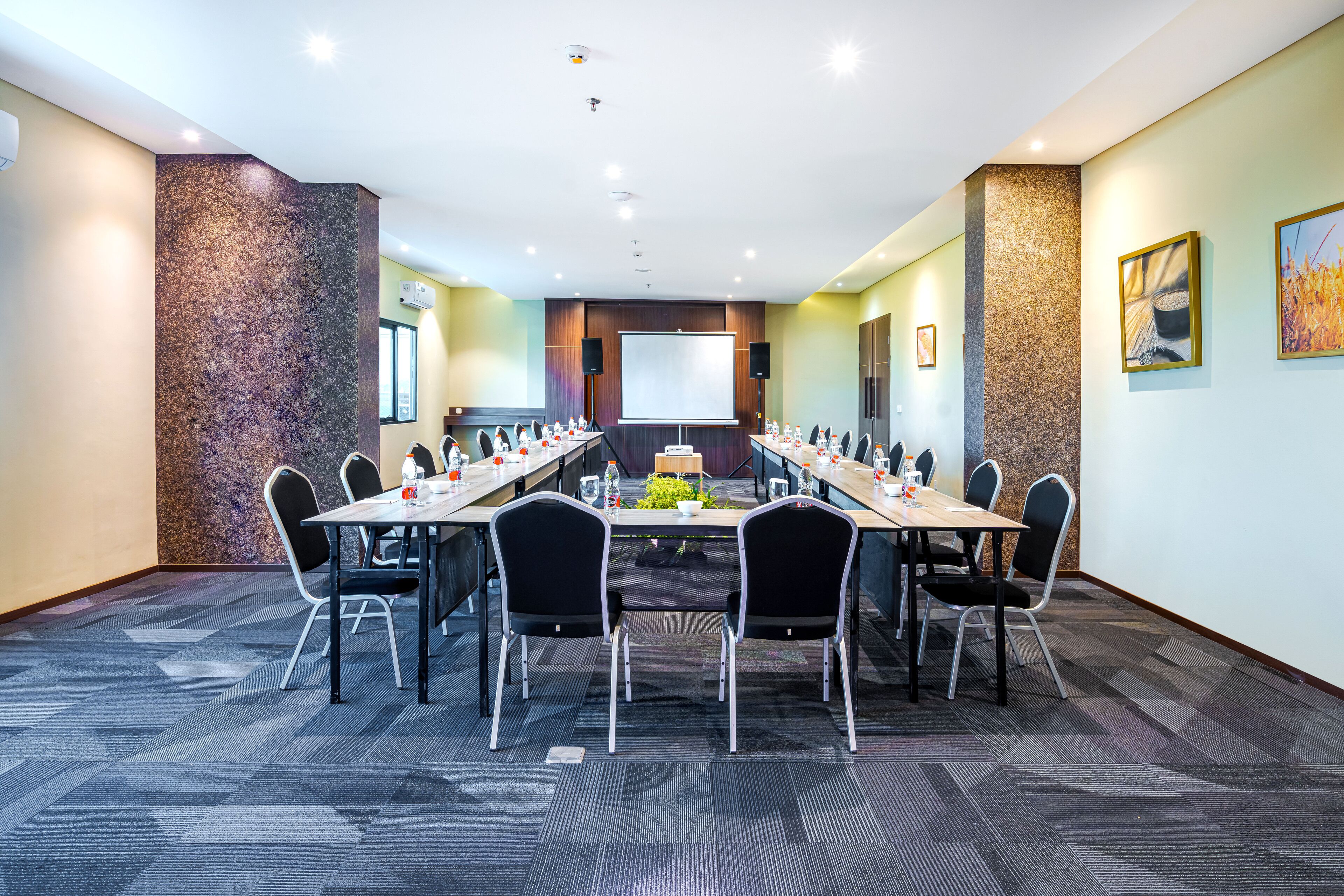 A conference room with a long table, chairs, a projector screen, and a carpeted floor.