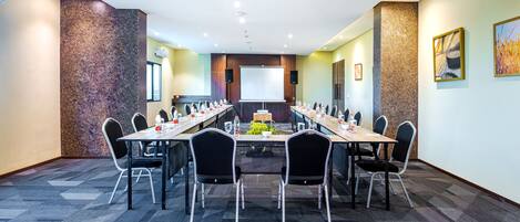 A conference room with a long table, chairs, a projector screen, and a carpeted floor.