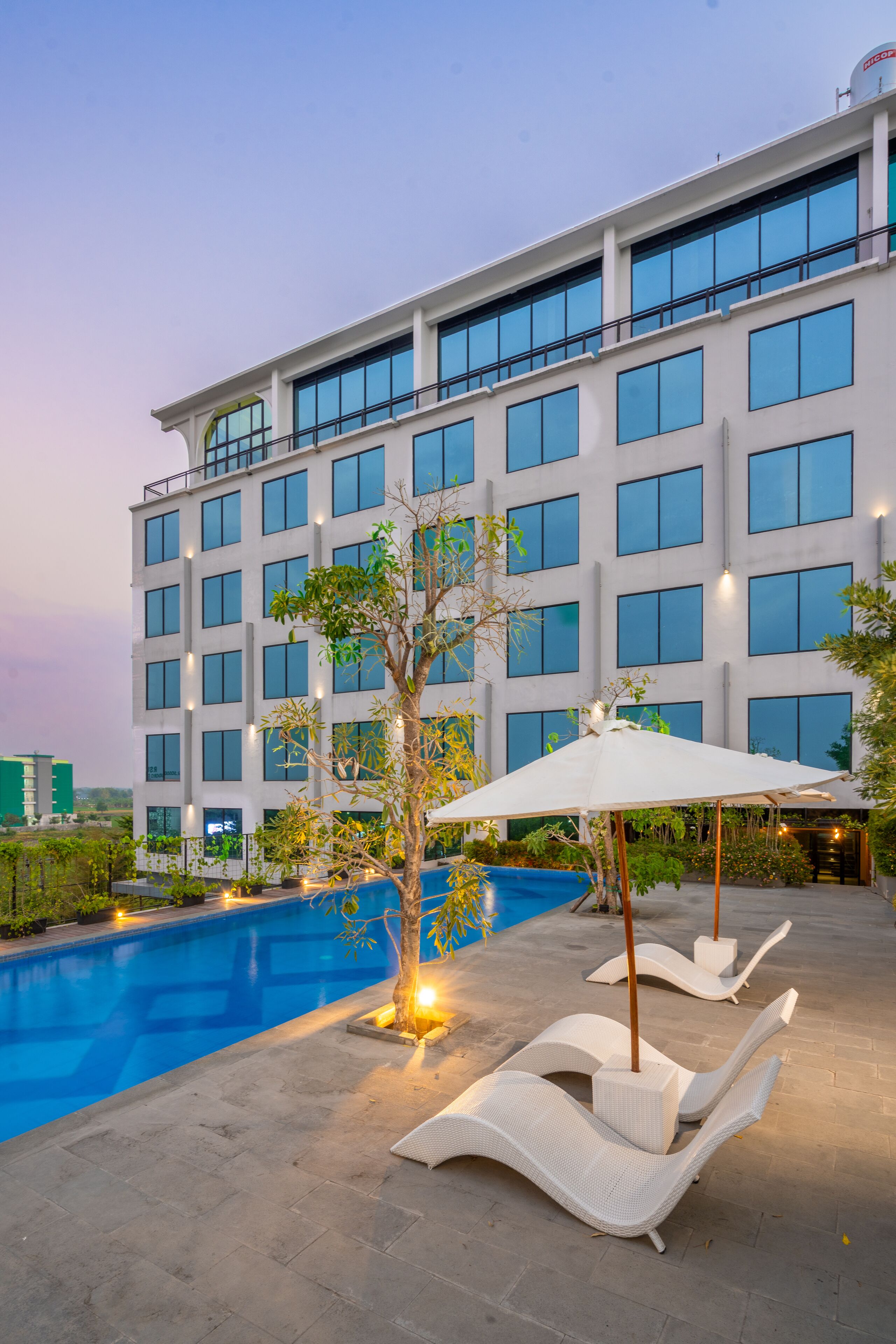 A modern hotel with a swimming pool, lounge chairs, and a well-lit outdoor area.