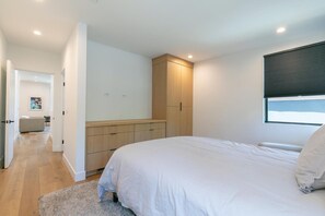 Une chambre à coucher comprenant un lit, une armoire, une fenêtre avec des stores et une porte donnant sur une autre pièce.