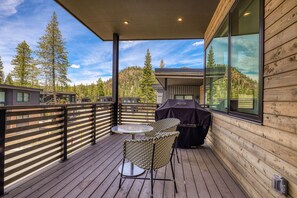 Une terrasse en bois avec une table et des chaises, un barbecue et une vue sur les arbres et les bâtiments.