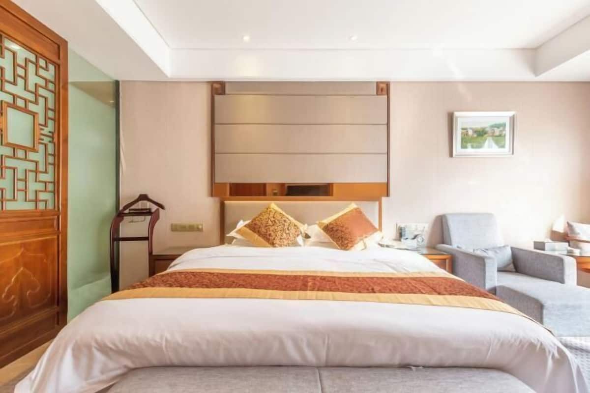 A hotel room with a bed, a chair, a desk, and a wall-mounted TV.