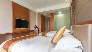 A hotel room with a large bed, a flat-screen TV mounted on the wall, and a wooden headboard.