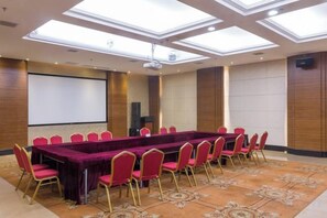 Une salle de conférence avec une longue table, des chaises rouges, un écran de projection et une grande fenêtre.