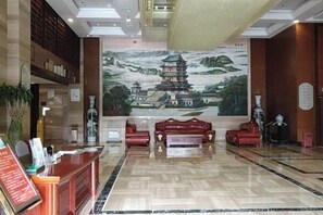 Un hall d’hôtel comprenant un comptoir d’accueil, un espace salon et une fresque représentant un bâtiment traditionnel.