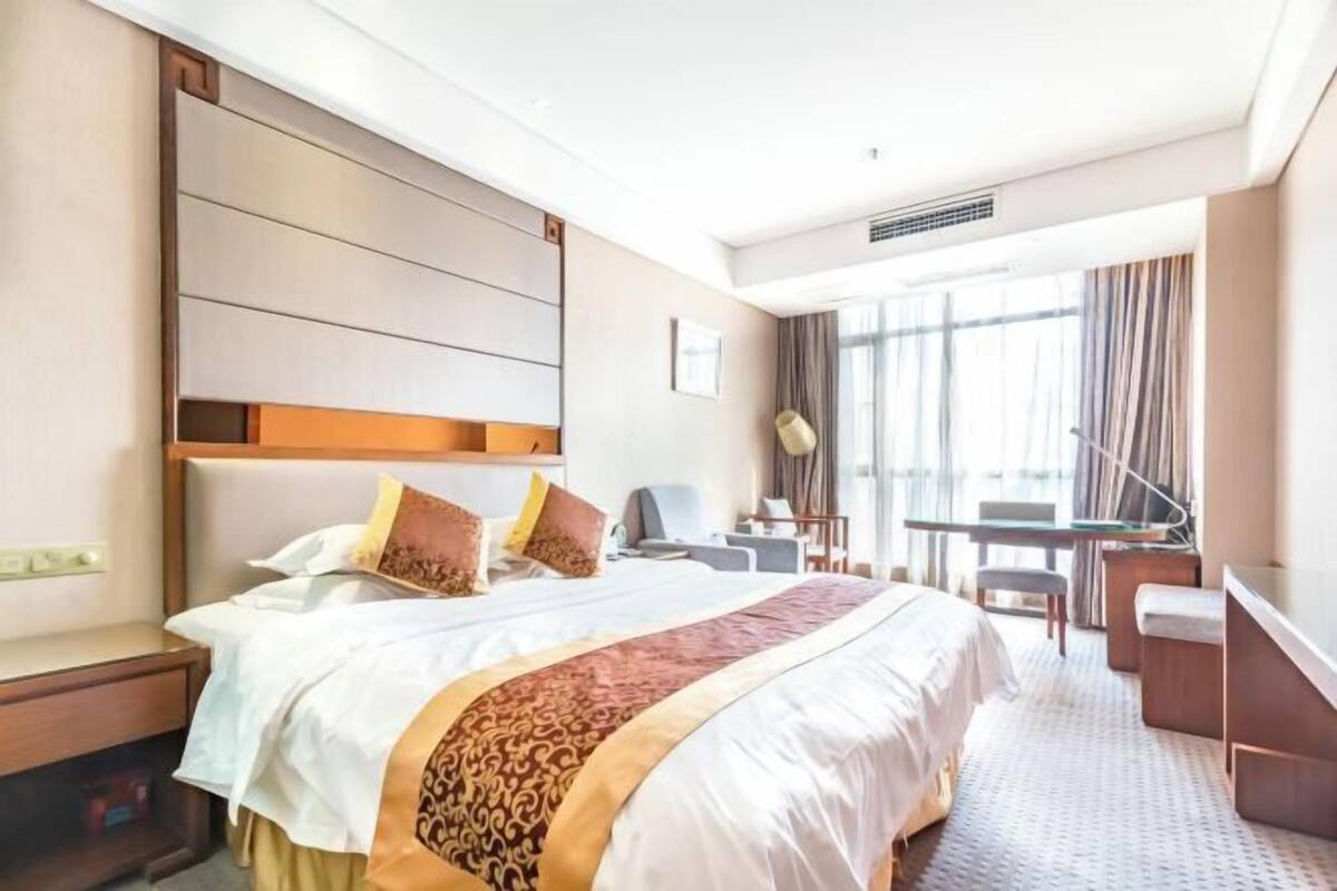 A hotel room with a large bed, a desk, and a chair.