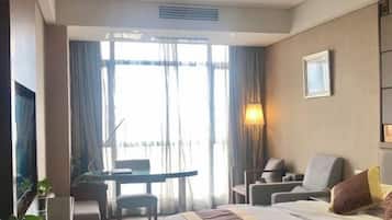 A hotel room with a bed, a desk, two chairs, a TV, and a window with curtains.