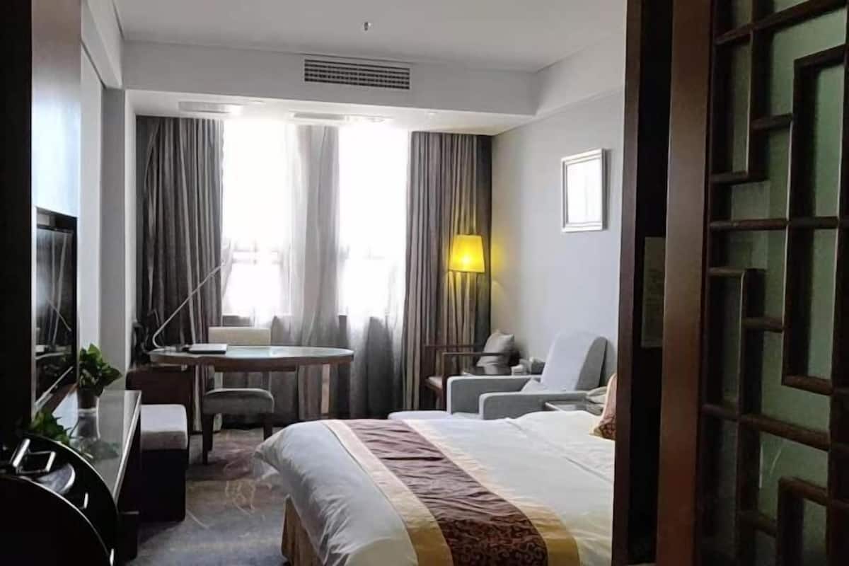 A hotel room with a bed, a desk, a chair, a TV, and a lamp.