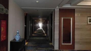 A hotel corridor with a carpeted floor, a vase on a table, and a door at the end.