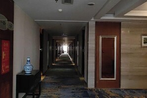Un couloir d’hôtel avec un sol recouvert de moquette, un vase posé sur une table et une porte au bout.