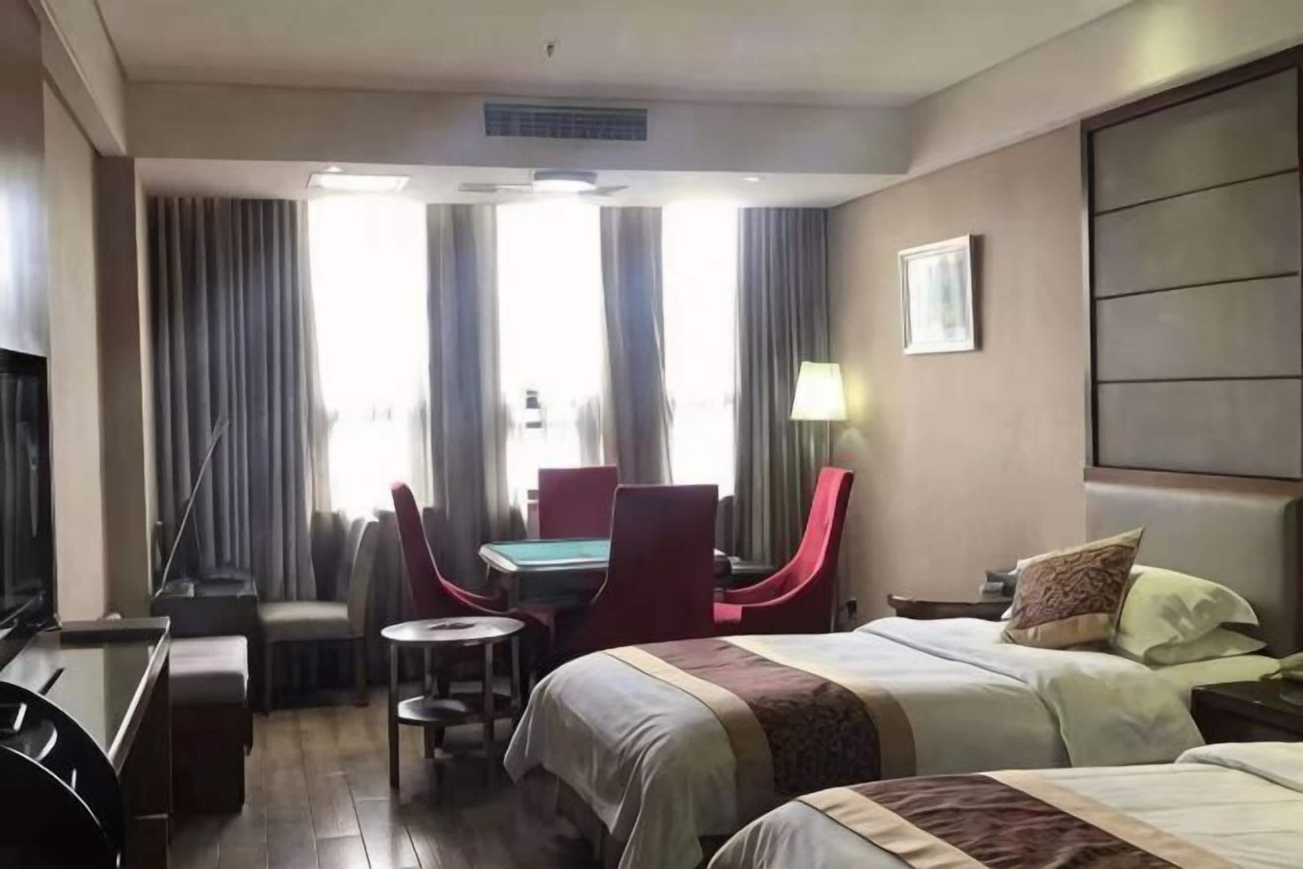 Ein Hotelzimmer mit Bett, Schreibtisch, Sessel, Fernseher und einem fenster mit Vorhängen.