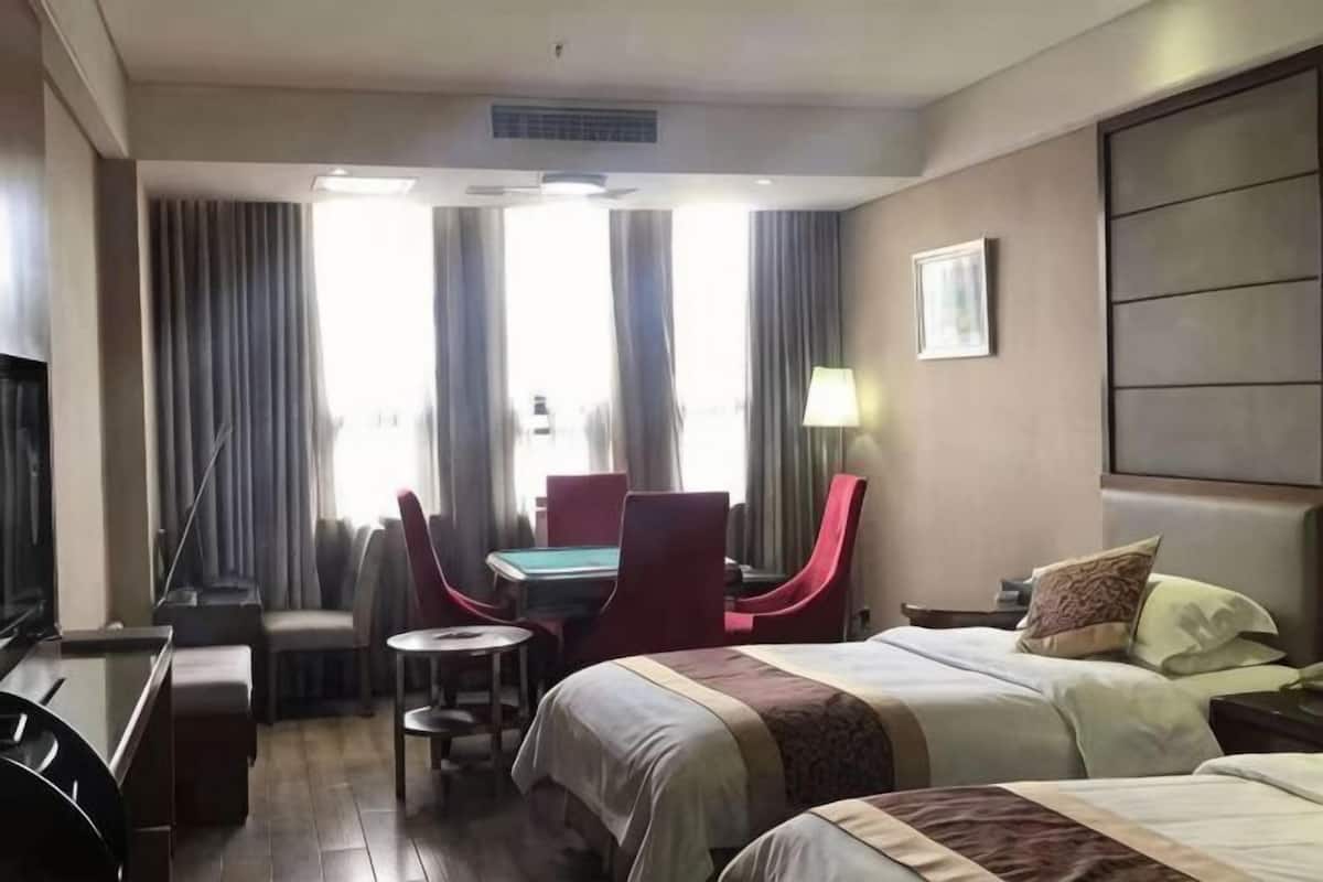 A hotel room with a bed, a desk, a chair, a TV, and a window with curtains.