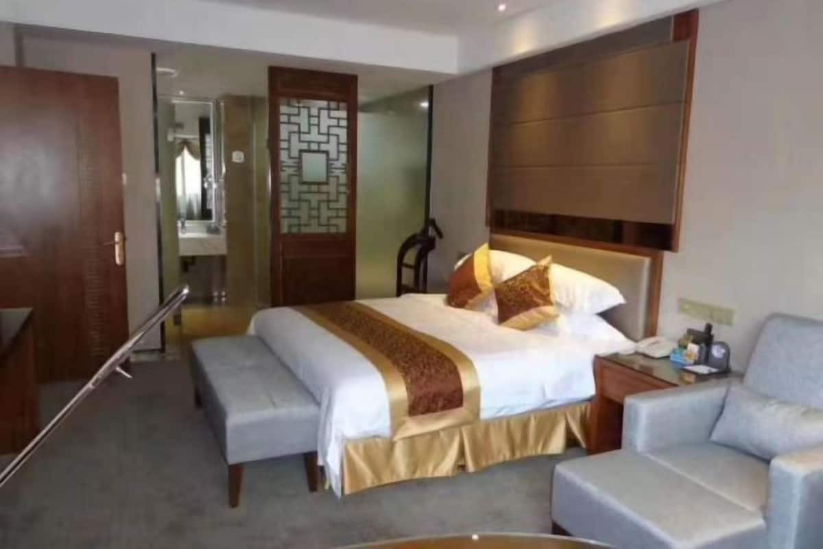 A hotel room with a large bed, a bedside table, a chair, and a mirror.