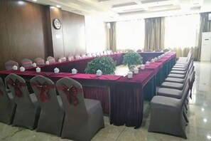 Un salón de conferencias con una larga mesa, sillas decoradas con lazos y un reloj en la pared.