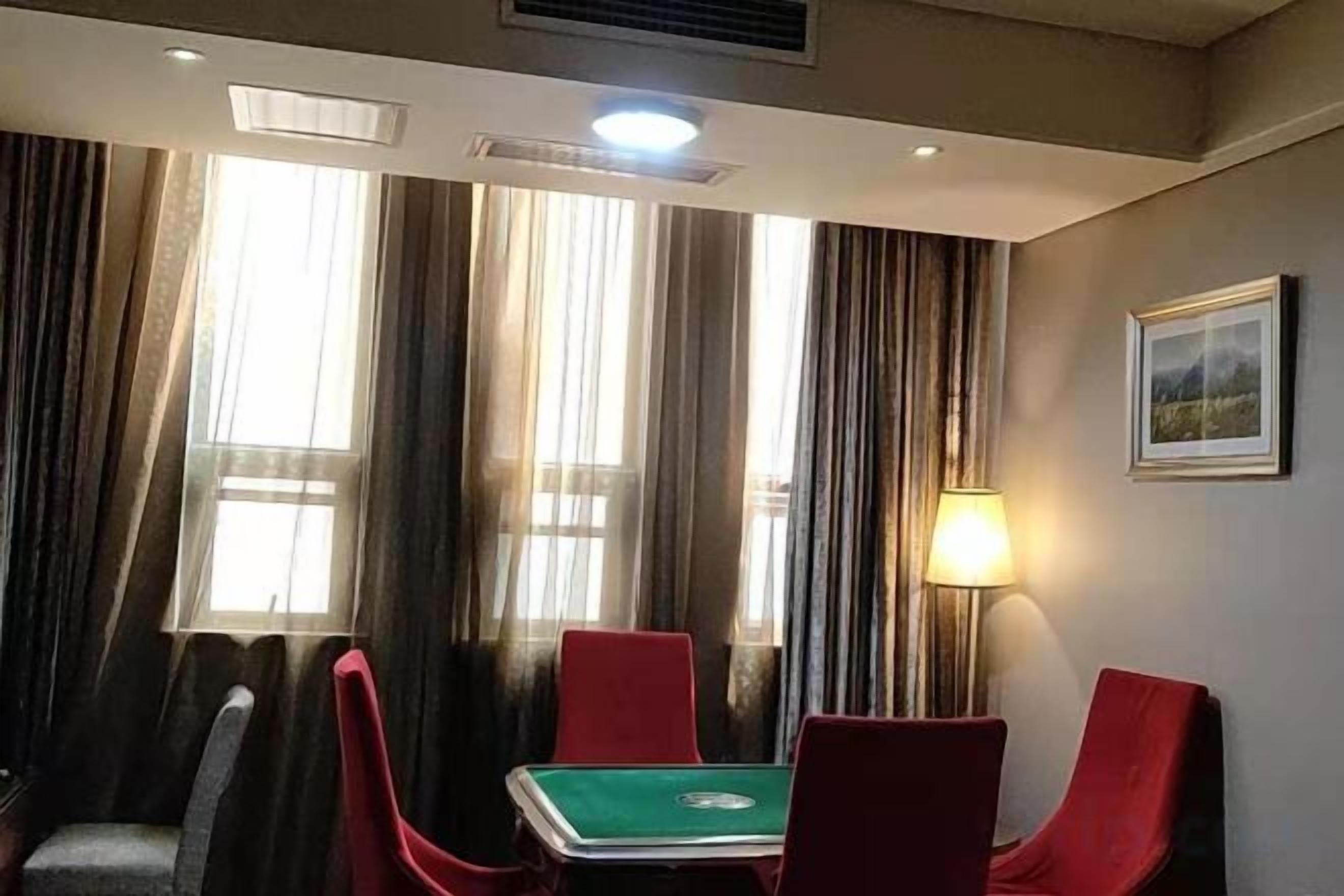 A room with a green table, red chairs, a lamp, and a framed picture on the wall.