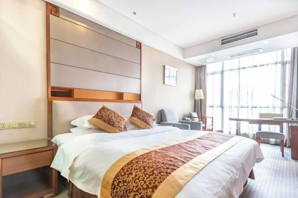 A hotel room with a large bed, a desk, a chair, and a window with curtains.