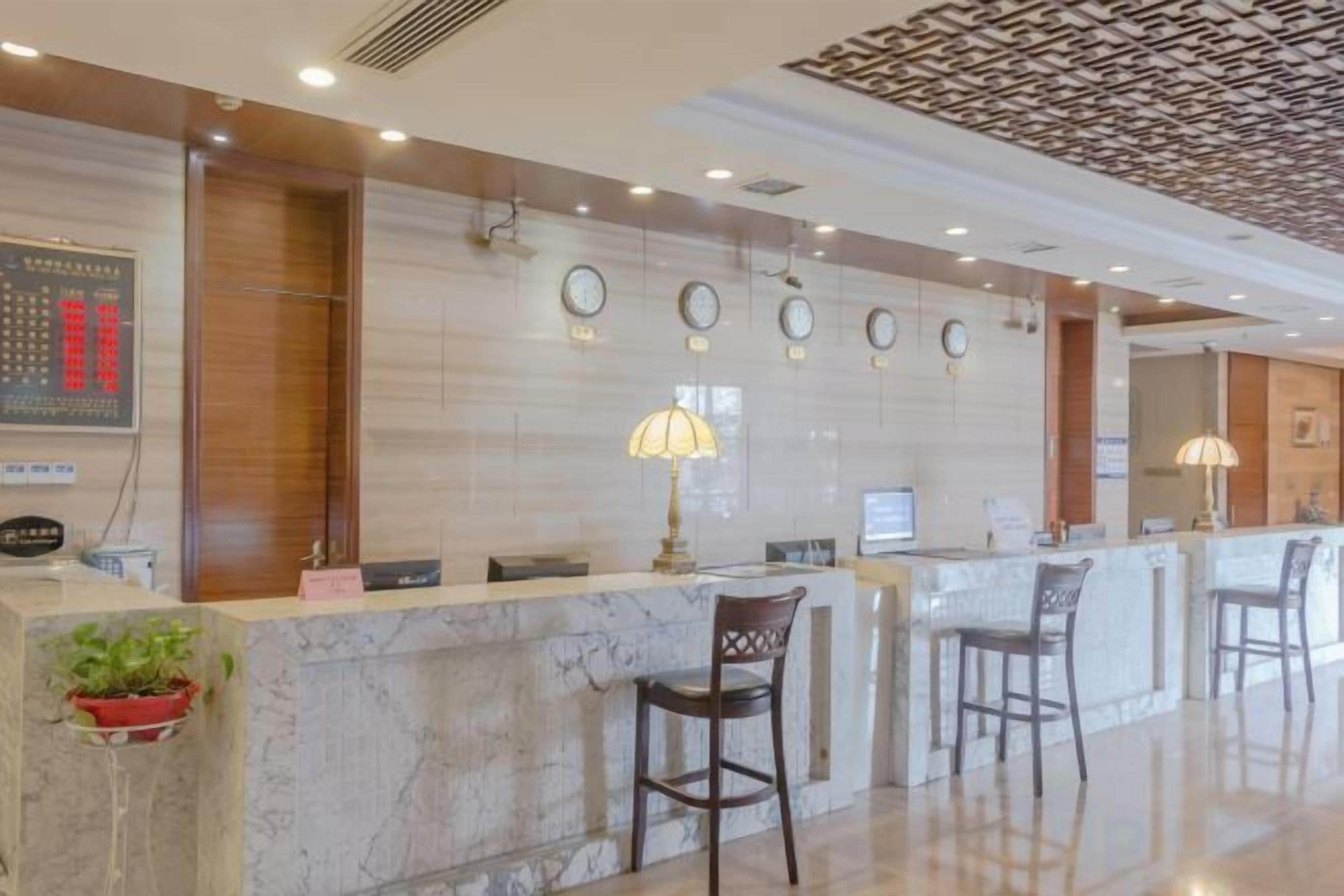 A hotel reception area with a marble counter, two chairs, a clock, and a decorative ceiling.