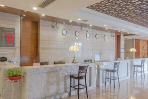 A hotel reception area with a marble counter, two chairs, a clock, and a decorative ceiling.