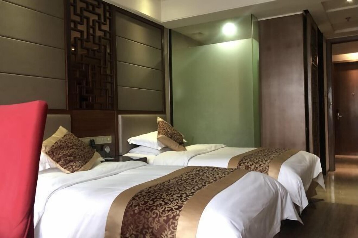 A hotel room with two beds, a wooden headboard, a green accent wall, and a red chair.