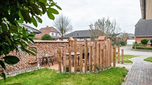 A brick wall with a wooden fence, a paved pathway, and a grassy area. - Apartment Krakow am See with Terrace & Wi-Fi (Krakow am See)