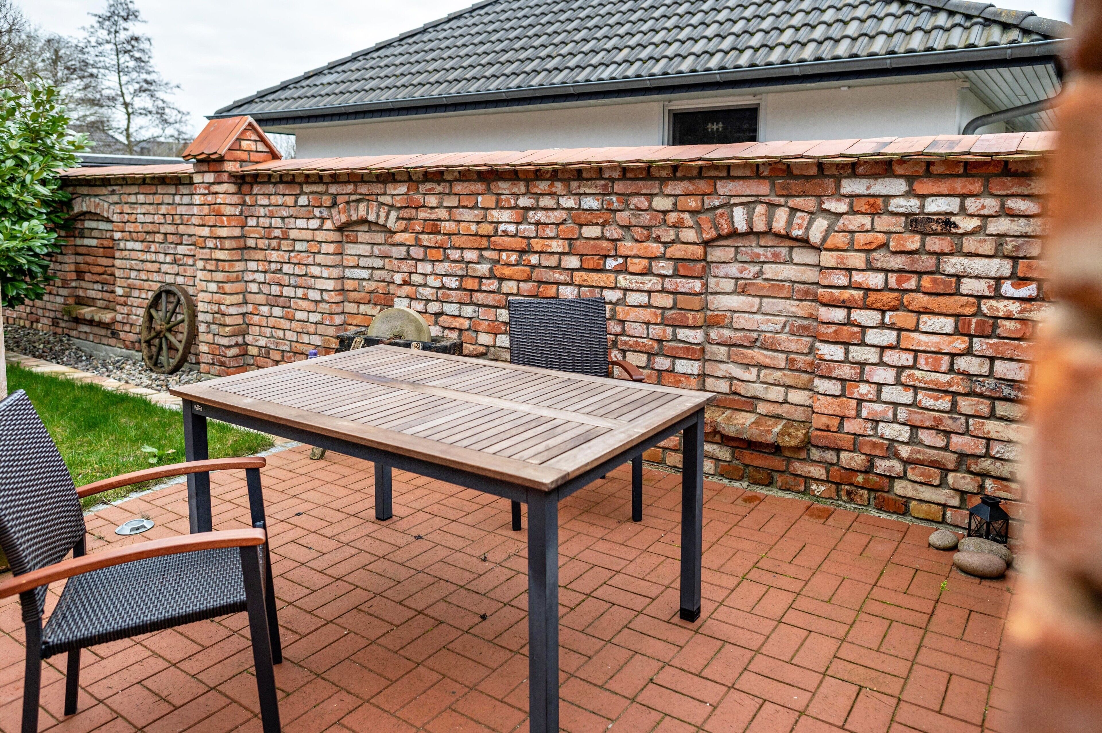 A patio with a brick wall, a table, and two chairs.