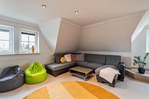 A loft-style living room with a sectional sofa, a bean bag, a coffee table, and a potted plant.