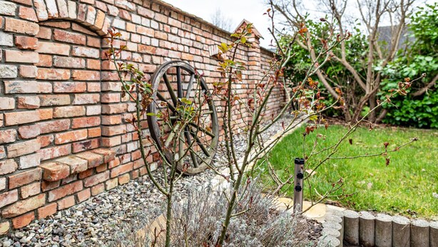Un mur de briques avec une grande roue, un petit arbre et une zone herbeuse.