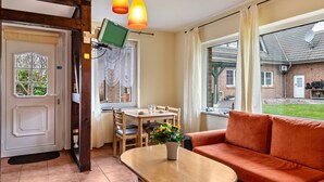 Une pièce avec une table en bois, un canapé, un téléviseur fixé au mur et une fenêtre avec des rideaux.