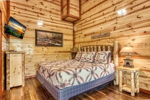 A wooden cabin bedroom with a bed, a nightstand, a lamp, a framed picture, and a sign on the wall.