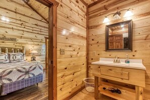 A wooden cabin interior with a bed, a wooden vanity with a mirror, and a small basket.