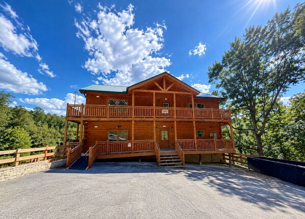 A two-story wooden cabin with a balcony, a covered porch, and a gravel driveway.