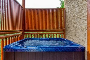 A hot tub with a wooden deck and a stone wall.