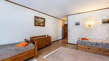 A room with two wooden beds, a wooden dresser, a wall-mounted light fixture, and a door leading to another room.
