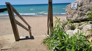 A beach with a wooden staircase leading down to the shore, a sign that reads 'STAY OFF ROCKS,' and some green vegetation in the foreground. - Dog-Friendly Farmhouse • Hot Tub • 1+ Acre • Near Beach, Golf, and Casino! (New Buffalo)