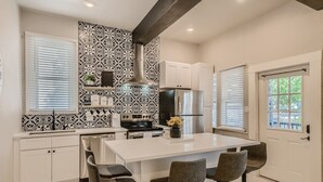 A modern kitchen with white cabinetry, a central island with bar stools, a stainless steel refrigerator, and a patterned backsplash.