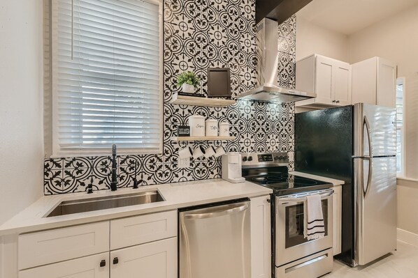 Una cocina con refrigerador de acero inoxidable, horno empotrado, lavavajillas y cafetera.