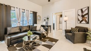 A modern living room with a sofa, armchair, and coffee table, a ceiling fan, and a view of the outside.
