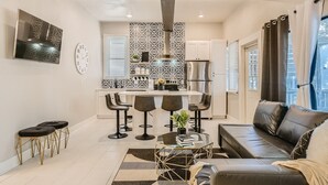 A modern kitchen with a central island, bar stools, a dining table, and a sofa in a living area.