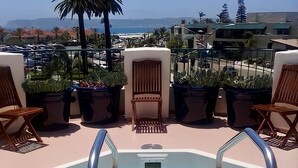 A rooftop pool area with lounge chairs and potted plants.