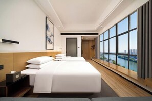 Habitació d'hotel moderna amb dos llits, una finestra gran amb vista a la ciutat, un paviment de fusta i un disseny minimalista.