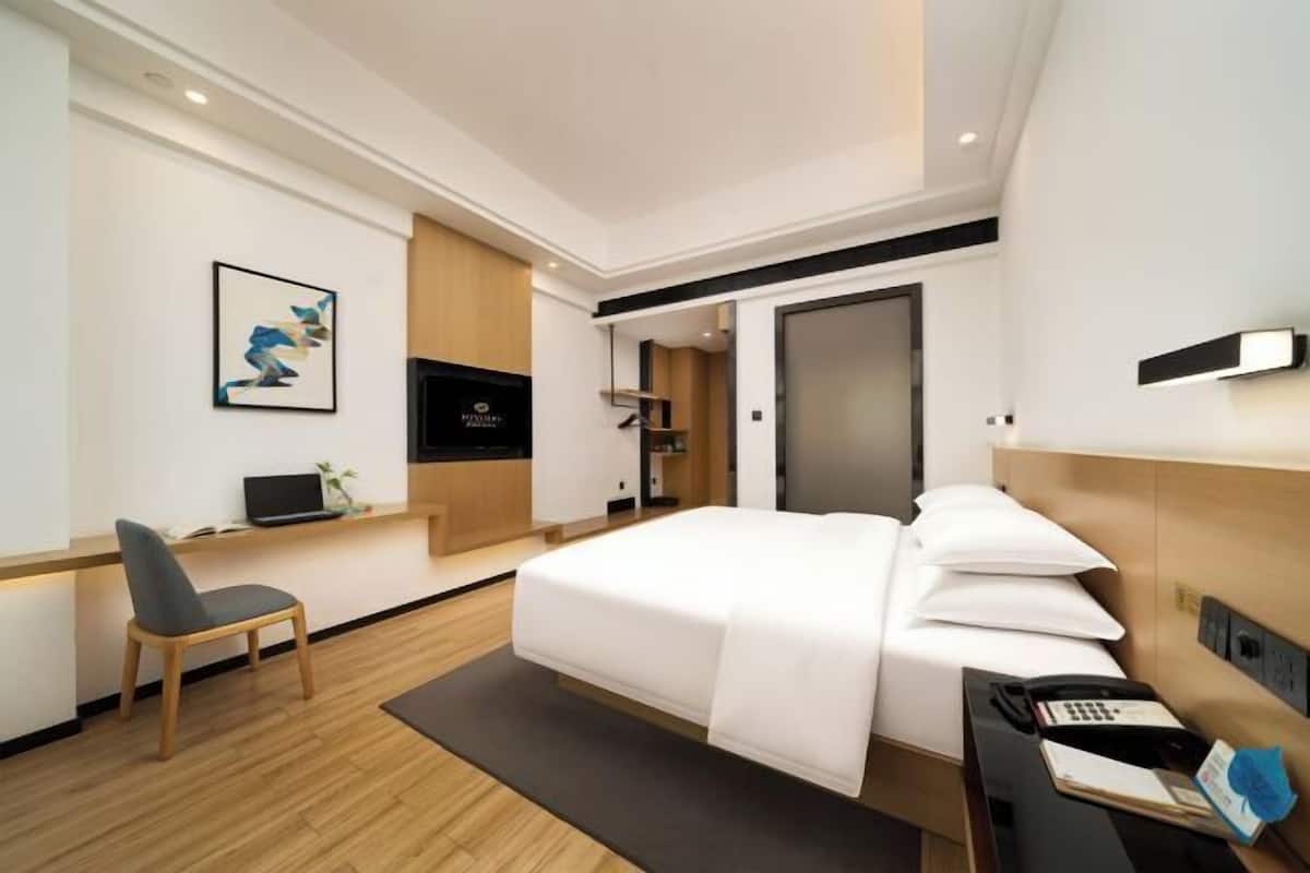 A modern hotel room with a bed, desk, chair, and a television.