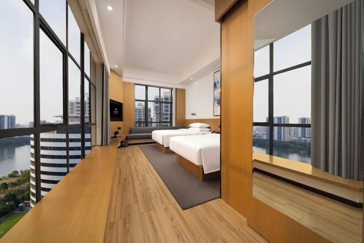 A modern hotel room with large windows, a wooden floor, a bed, and a TV.