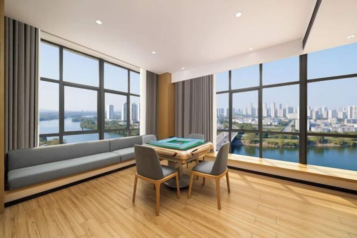 A modern room with large windows, a wooden floor, a sofa, and a table with chairs.