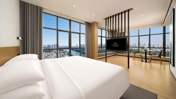 Een moderne hotelkamer met een groot bed, een televisie, een balkon met uitzicht op de stad, en een groot raam.