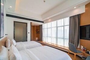 Habitación de hotel con dos camas, televisión, una silla y un ventanal grande con cortinas.