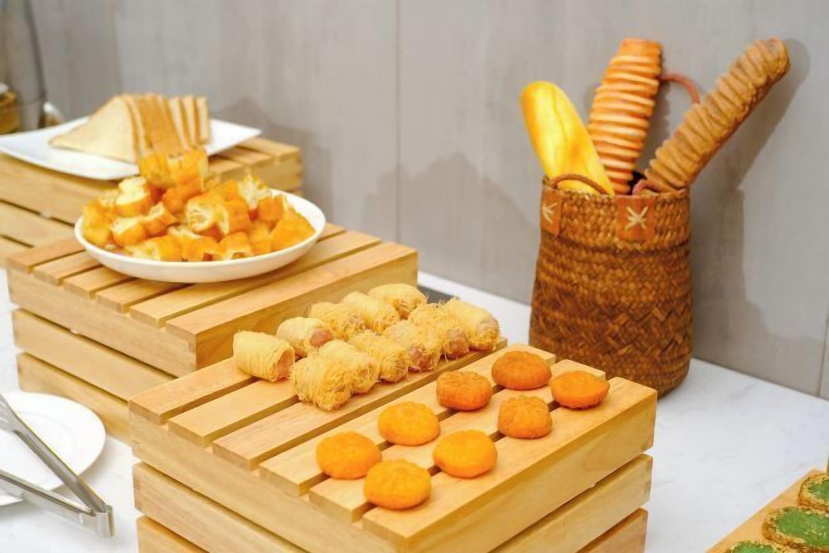 A buffet table with various food items, including bread, pastries, and a basket with baguettes.